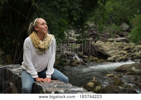 Happy young girl sitting by the river rocks in a forest enjoying the quietness