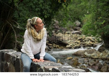 Happy young girl sitting by the river rocks in a forest enjoying the quietness