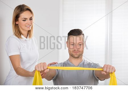 Close-up Of A Young Female Physiotherapist Giving Man A Training With Exercise Band