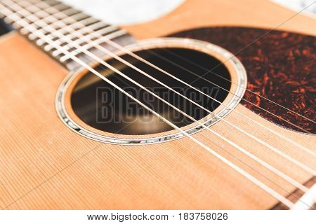 Close up of steel strings on an acoustic guitar. Cedar top with textured pickguard and ornate design around sound hole.