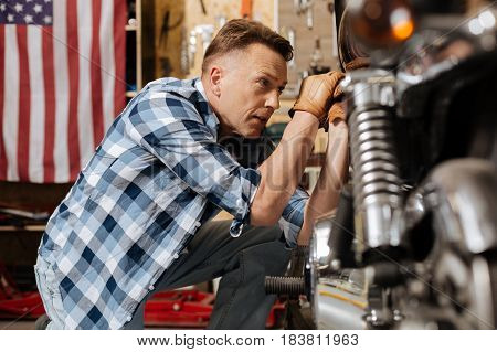 Attention to details. Attractive scrupulous master serviceman fulfilling a new order and repairing vintage motorbike while tightening a bolt