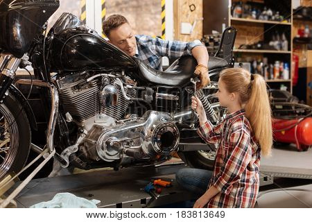 Best assistant. Enchanting lovely curios daughter and her dad enjoying their weekend while the dad fixing his motorbike and the daughter assisting him