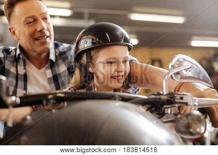 Can you feel the power. Lively clever curious child visiting her dad at work and feeling enthusiastic about it while he sitting her on one of his vehicles