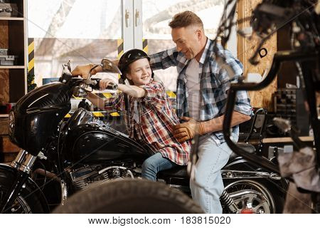 Take on a ride. Cheerful happy admirable kid sitting on dads bike while he taking a break and showing her around his workplace