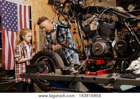 Expert dad. Gifted competent able mechanic explaining his child how separate part of the bike working while she spending time at his garage