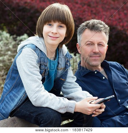 Father with teen son using smart phone outdoor together. Young boy with his father in spring park.