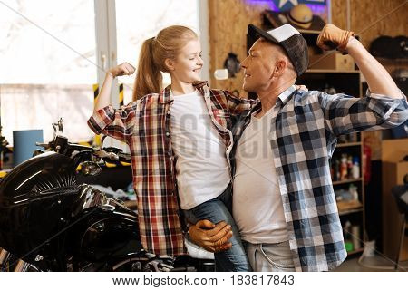 My little Hercules. Charming sincere lovely girl and her parent figuring out which one of them being stronger while enjoying their time in dads workshop