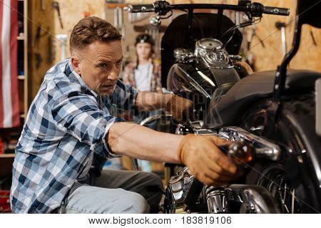 Last touches. Intelligent diligent reliable man making sure the lights working fine while running a checkup on his bike and his daughter waiting for him
