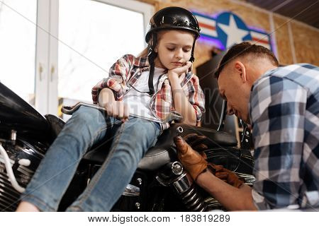 Trained scrupulous mature man looking at the tool and wondering whether it fitting the bolt or not while his child watching him attentively