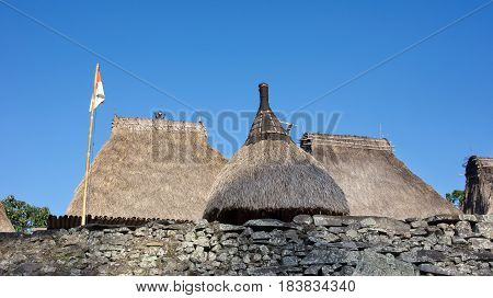 Three grass rooftops and Indonesian flag at Bena a traditional village with grass huts of Ngada people in Flores near Bajawa Indonesia.
