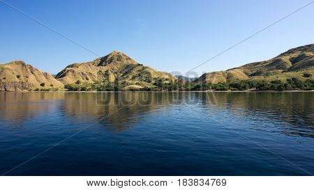 Coastline of mountains with green vegetation reflected in blue ocean water at Labuan Bajo in Flores Indonesia.