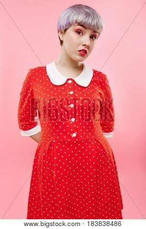 Close up portrait of beautiful dollish girl with short light violet hair wearing red dress over pink background. Copy space.