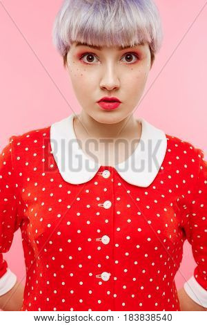 Close up portrait of beautiful dollish girl with short light violet hair wearing red dress over pink background. Copy space.