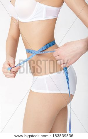 young woman measuring her perfect slim body iwith a blue measuring tape over white background