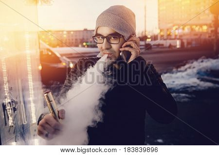 vaping man holding a mod device with phone. Concept information technology. cloud of vapor. Vape. high contrast and monochrome color tone.