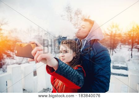 Vape guy and girl - lovers at sunset look in the phone and laugh. The concept of refusal of tobacco.Selfie
