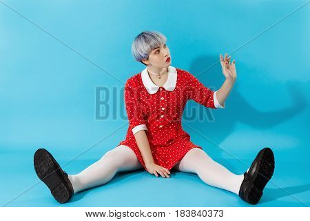 Picture of beautiful dollish girl with short light violet hair wearing red dress over blue background. Copy space.
