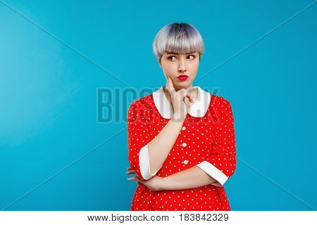 Close up portrait beautiful dollish girl with short light violet hair wearing red dress over blue background. Copy space.