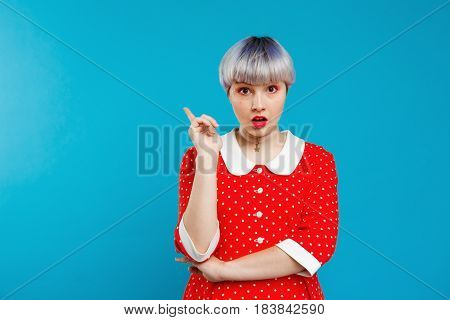 Close up portrait upset beautiful dollish girl with short light violet hair wearing red dress over blue background. Copy space.