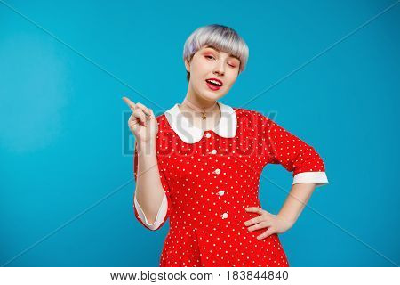 Close up portrait beautiful dollish girl with short light violet hair wearing red dress over blue background. Copy space.