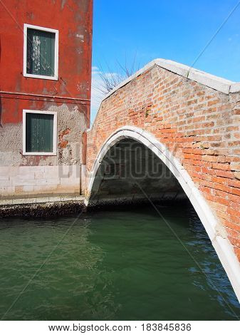 footbridge in murano venice with red building and peeling paint