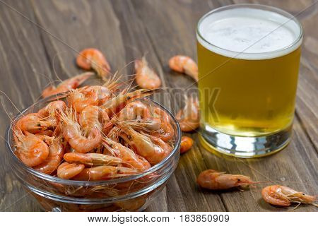 Glass of beer with boiled shrimps in a glass bowl on wooden background, from angle