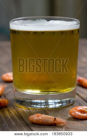 Glass of fresh cold beer on wooden surface with boiled shrimps, close-up
