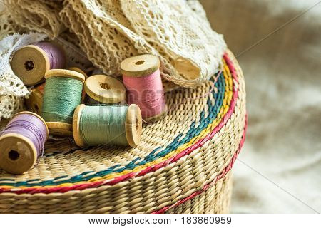 Woven rattan crafts and sewing supply box wooden spools rolls of lace linen cloth background hobby fashion concept close up
