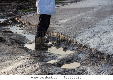 Human feet shod in rubber boots standing in a muddy rut