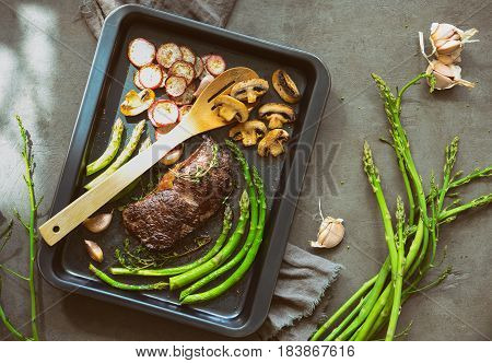 Beef and roasted radishes and asparagus and some mushrooms in a sheet pan lighten up by spring sunshine high angle view