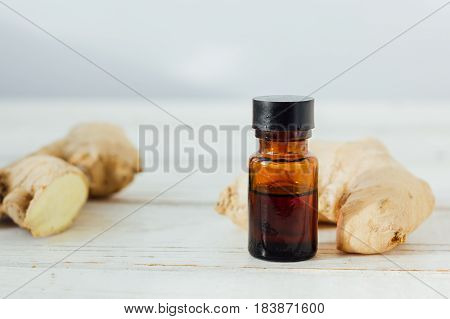 Ginger Essential Oil In Glass Bottle With Ginger Root Behind.