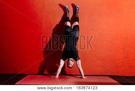Athlete doing push ups on his hands while standing upside down near red wall. Full body length portrait