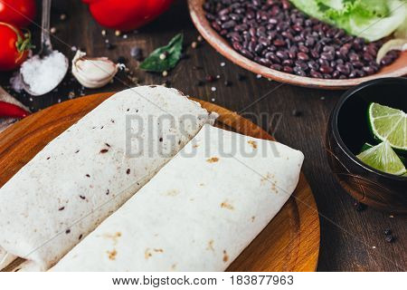 Vegetarian Burrito On Wooden Board Over Black Table Surrounded By Ingredients.