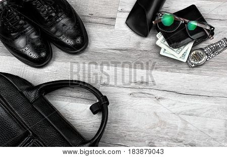 Man accessories in business style. Briefcase, brogues , shoes, wallet with money and other luxury businessman attributes on leather black background, fashion industry, top view.Copy space