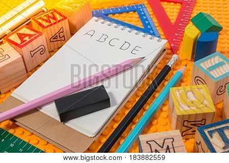 Blank notebook with word ABC and school supplies on yellow plastic brick plate. Learning background concept.
