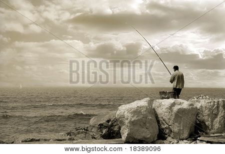 Old fisherman standing on the breakwater with fishing rod (sepia toned).