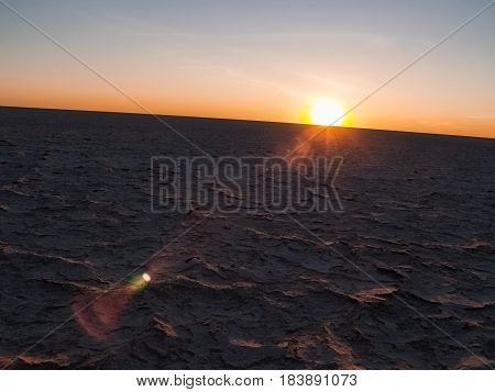 Sun on curved horizon over baked dry cracked crust of Makgadikgadi Pans National Park scenic large flat area of salt pan desert of Botswana