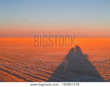 Shimmering horizon and long shadows as sun sets across Makgadikgadi Pans National Park scenic large flat area of salt pan desert of Botswana