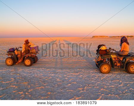 Makgadikgadi, Botswana -August 29, 2007; Tourist and guide in glow of setting sun on quad bikes stop while crossing Makgadikgadi Pans National Park scenic large flat area of salt pan desert to take in view Botswana