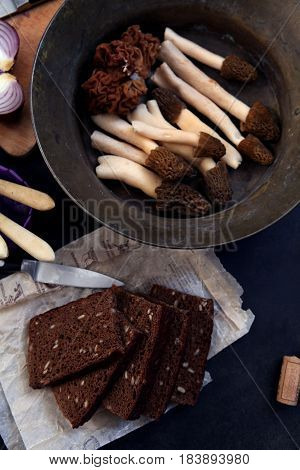 Still llife with raw morels, onion, and rye bread on the dark background