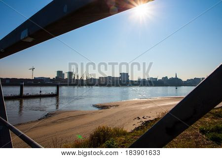 The sun shinging in the blue summersky over the river and the riverside as seen from the other side of the river