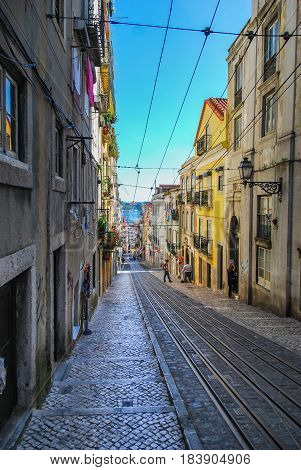 Steep narrow street of Lisbon with cable car rails in the middle and ocean in the background