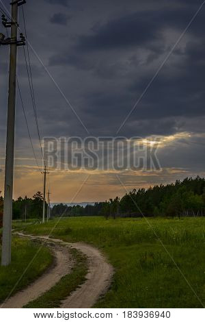 Road crosses a meadow covered by clouds into rays of sun.