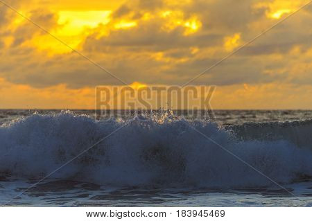 Magic dramatic sunset on the beach by the ocean. Silhouettes of a wave and clouds on a color sky during sunset. Evening on a tropical beach. Travel to the sea.