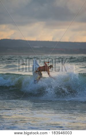 Surfer with a tanned body performs a trick on a short board - a jump over the waves. Extreme water sports, fun at the oceanfront surfing. The surfer rolls on the waves at sunset.