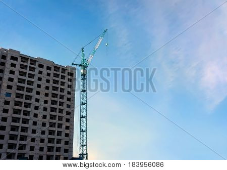 Tower crane and building under construction against blue sky. Copy space photo of the construction