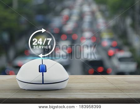 24 hours service icon with wireless computer mouse on wooden table over blur of rush hour with cars and road Full time service concept