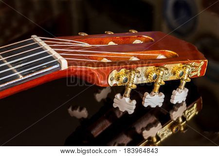 Guitar headstock on black reflecting surface close up with very shallow depth of field focus on tuning pegs