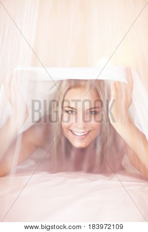Joyful woman having fun in the bed, lying down behind transparent valance, enjoying romantic interior of bedroom, happy healthy lifestyle