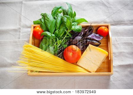 Green and purple basil chunk of parmesan cheese raw cappellini and tomatoes on wooden tray